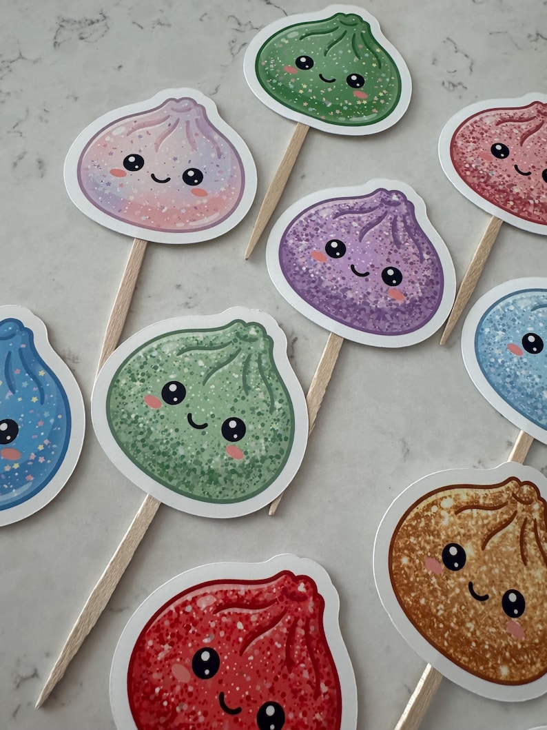 May include: A collection of decorative food toppers featuring various colorful, glittery dumpling illustrations with smiling faces. Each dumpling is attached to a wooden pick, showcasing shades of green, purple, pink, blue, and brown with sparkling details.