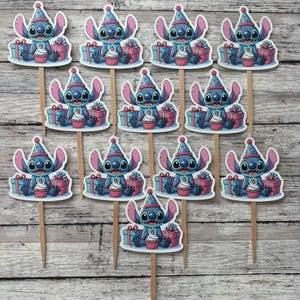 May include: Twelve blue and white cupcake toppers featuring Stitch from Lilo & Stitch wearing a party hat and holding a cupcake with a candle. The toppers are on wooden sticks and are surrounded by presents.
