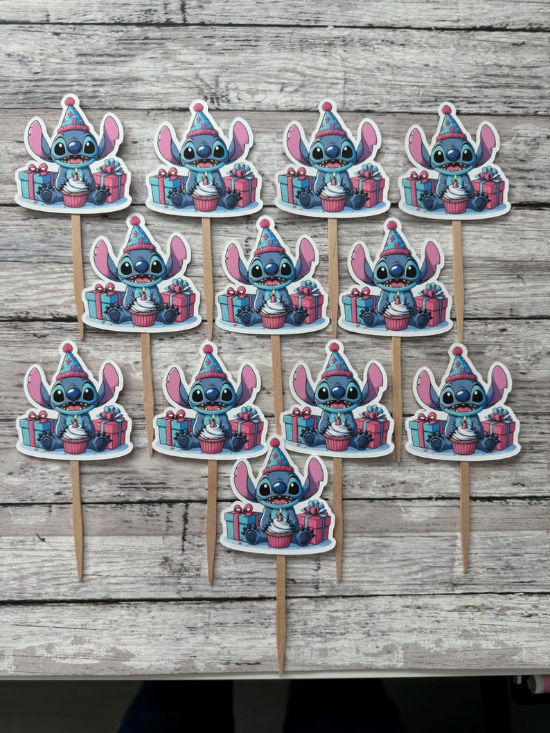 May include: Twelve blue and white cupcake toppers featuring Stitch from Lilo & Stitch wearing a party hat and holding a cupcake with a candle. The toppers are on wooden sticks and are surrounded by presents.