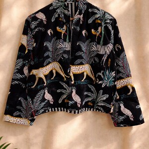 K&ouml;nnte beinhalten: Schwarze Jacke mit einem lebendigen Dschungel-Print mit Geparden, Zebras, Papageien und Palmen. Die Jacke hat einen Kragen und lange &Auml;rmel. Die Manschetten und der Saum sind mit einem wei&szlig;-schwarzen Streifenmuster versehen.