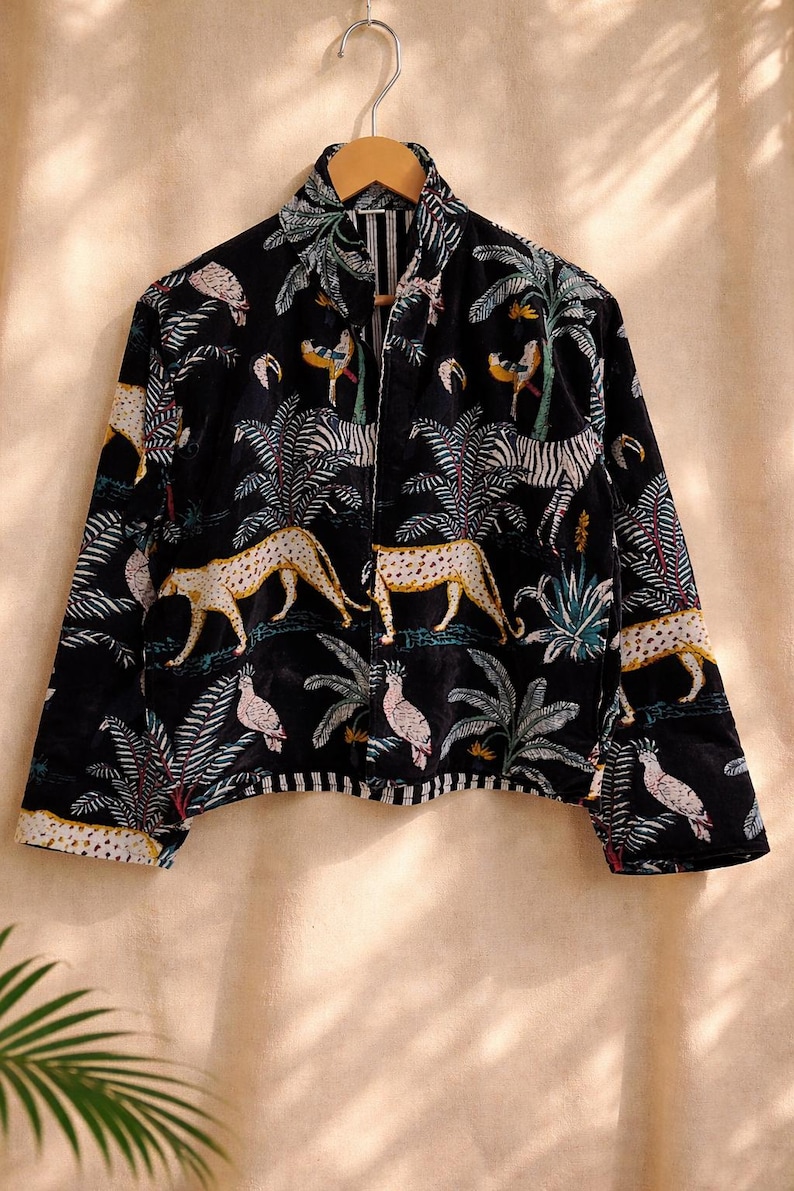 K&ouml;nnte beinhalten: Schwarze Jacke mit einem lebendigen Dschungel-Print mit Geparden, Zebras, Papageien und Palmen. Die Jacke hat einen Kragen und lange &Auml;rmel. Die Manschetten und der Saum sind mit einem wei&szlig;-schwarzen Streifenmuster versehen.