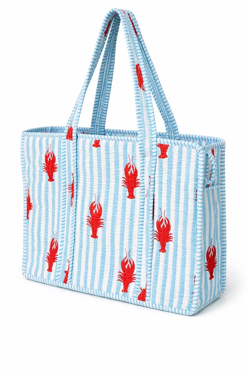 May include: A rectangular tote bag with blue and white vertical stripes and red lobster illustrations. The bag has matching striped handles and trim. The bag is made of a textured fabric.