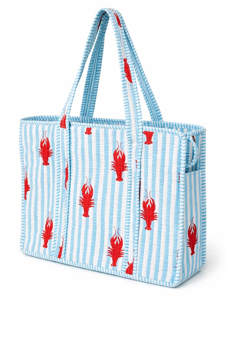 May include: A blue and white striped tote bag with red lobster designs. The bag has two handles and a side pocket. The bag is made of a textured fabric.
