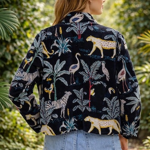 K&ouml;nnte beinhalten: Schwarze Jacke mit einem Dschungel-Print, der Zebras, Leoparden und V&ouml;gel inmitten tropischer Pflanzen zeigt. Die Jacke hat einen Kragen und lange &Auml;rmel. Das Model tr&auml;gt hellblaue Jeansshorts.