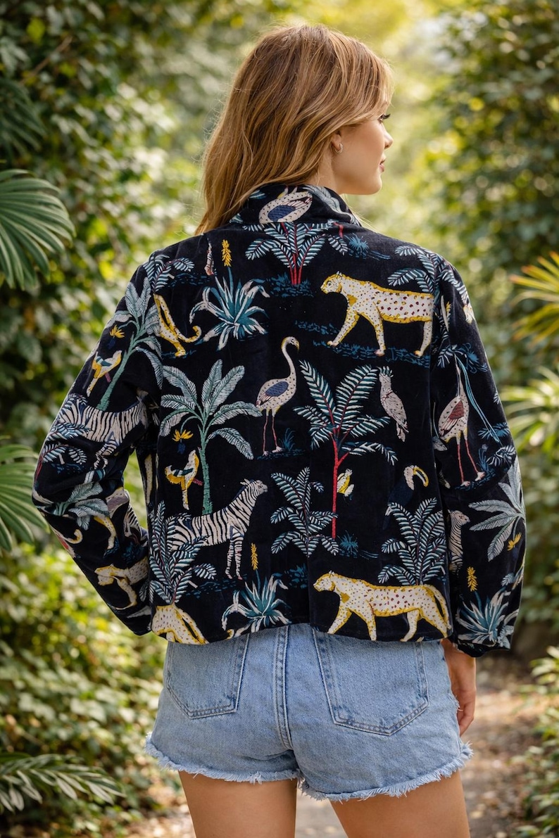 K&ouml;nnte beinhalten: Schwarze Jacke mit einem Dschungel-Print, der Zebras, Leoparden und V&ouml;gel inmitten tropischer Pflanzen zeigt. Die Jacke hat einen Kragen und lange &Auml;rmel. Das Model tr&auml;gt hellblaue Jeansshorts.