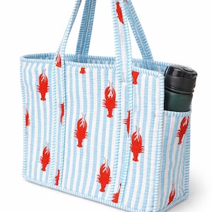 May include: A blue and white striped tote bag with a red lobster pattern. The bag has a pocket on the side and a green water bottle inside. The handles and trim are blue and white striped.