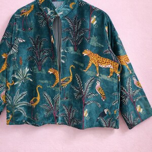 May include: Teal velvet jacket with a jungle-themed print. The jacket features a repeating pattern of leopards, zebras, flamingos, toucans, and monkeys among palm trees. The collar and cuffs have a yellow and brown pattern. The inside lining has a black and white striped pattern.