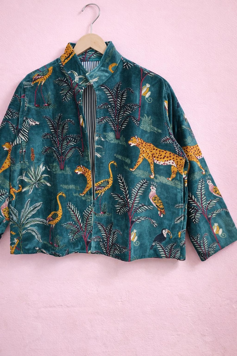 May include: Teal velvet jacket with a jungle-themed print. The jacket features a repeating pattern of leopards, zebras, flamingos, toucans, and monkeys among palm trees. The collar and cuffs have a yellow and brown pattern. The inside lining has a black and white striped pattern.