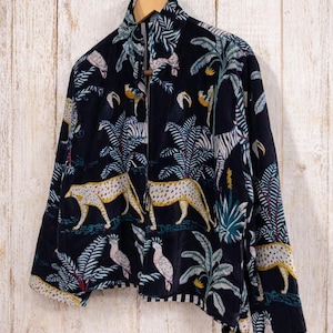 K&ouml;nnte beinhalten: Marineblaue Jacke mit Rei&szlig;verschluss und einem lebendigen Dschungel-Print mit Leoparden, Zebras, Papageien und Palmen. Die Jacke h&auml;ngt an einem Holzb&uuml;gel vor einer hellen Holzpaneelwand. Die Jacke hat einen hohen Kragen.