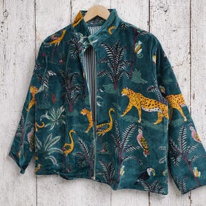 May include: Teal velvet jacket with a jungle-themed print. The jacket features a zipper closure and a collar. The print includes leopards, birds, and palm trees. The interior lining has a striped pattern.