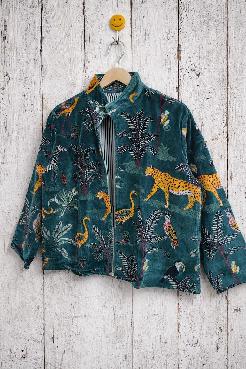 May include: Teal velvet jacket with a jungle-themed print. The jacket features a zipper closure and a collar. The print includes leopards, birds, and palm trees. The interior lining has a striped pattern.