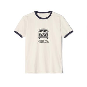 May include: Cream-colored t-shirt with navy blue trim featuring a black and white graphic of a vintage VW bus. The text "I HAVE A SPLIT PERSONALITY" is printed below the bus. The shirt has short sleeves.