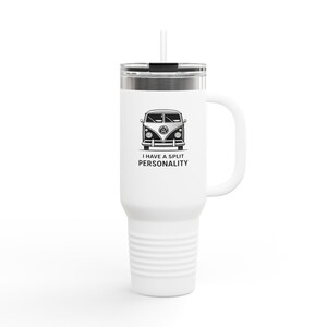 May include: White travel mug with a black and white graphic of a vintage VW bus and the text "I HAVE A SPLIT PERSONALITY". The mug has a handle, a silver lid, and a white straw. The mug is designed to hold hot or cold beverages.
