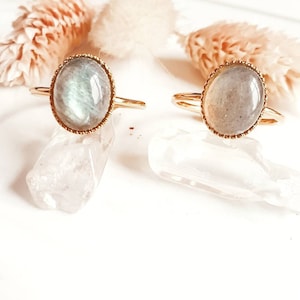 May include: Two gold rings with oval-shaped labradorite gemstones. The rings are set on a white surface with clear quartz crystals.