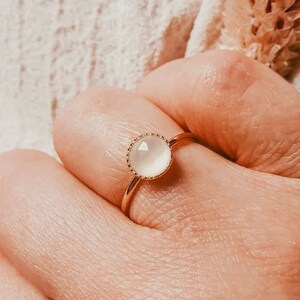 May include: A gold ring with a white gemstone. The ring has a delicate, scalloped edge around the stone.