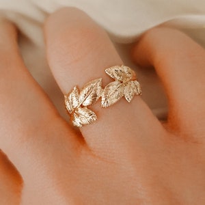 May include: A gold ring with a design of leaves. The ring is on a person's finger.