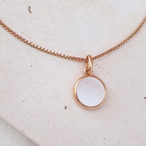 Op de afbeelding: Een gouden ketting met een ronde witte parelmoer hanger.