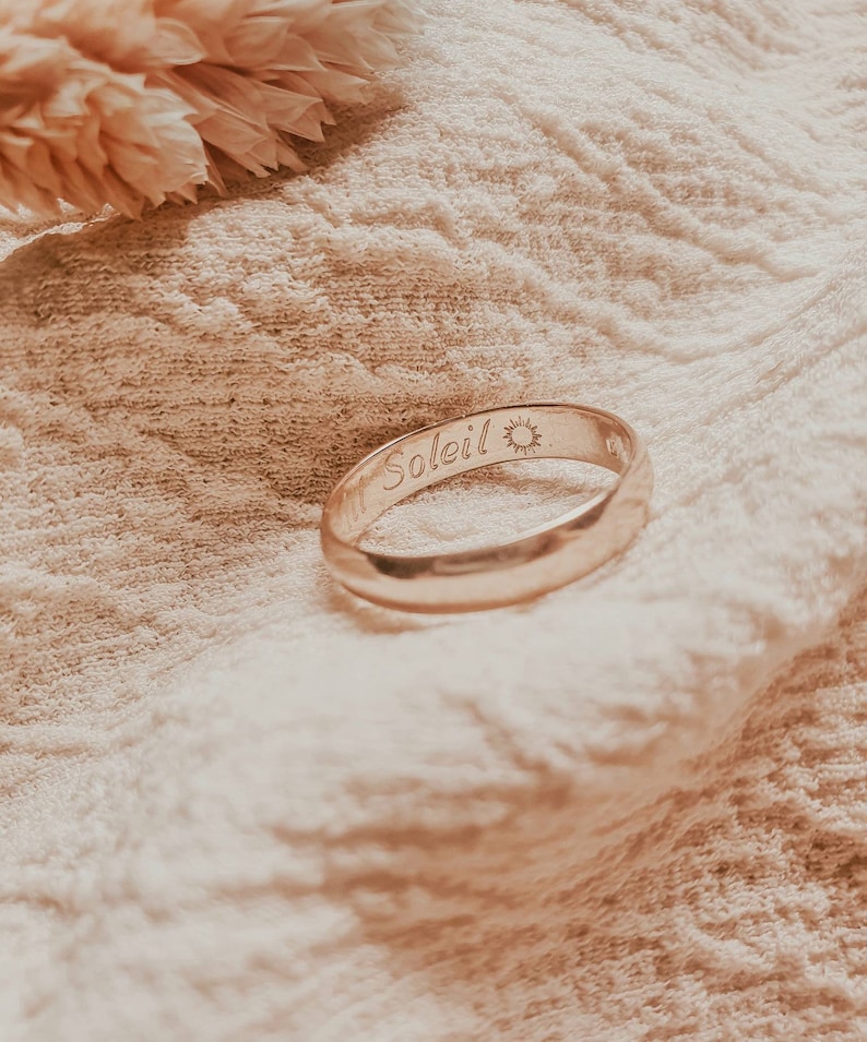 Pu&ograve; includere: Un anello a fascia d'oro con la parola "Soleil" e un simbolo di sole inciso all'esterno.