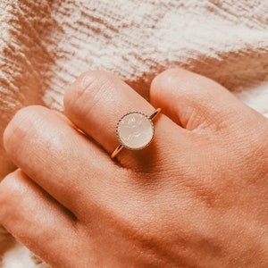 May include: A gold ring featuring a white, carved gemstone set in a gold bezel. The stone has a floral design.