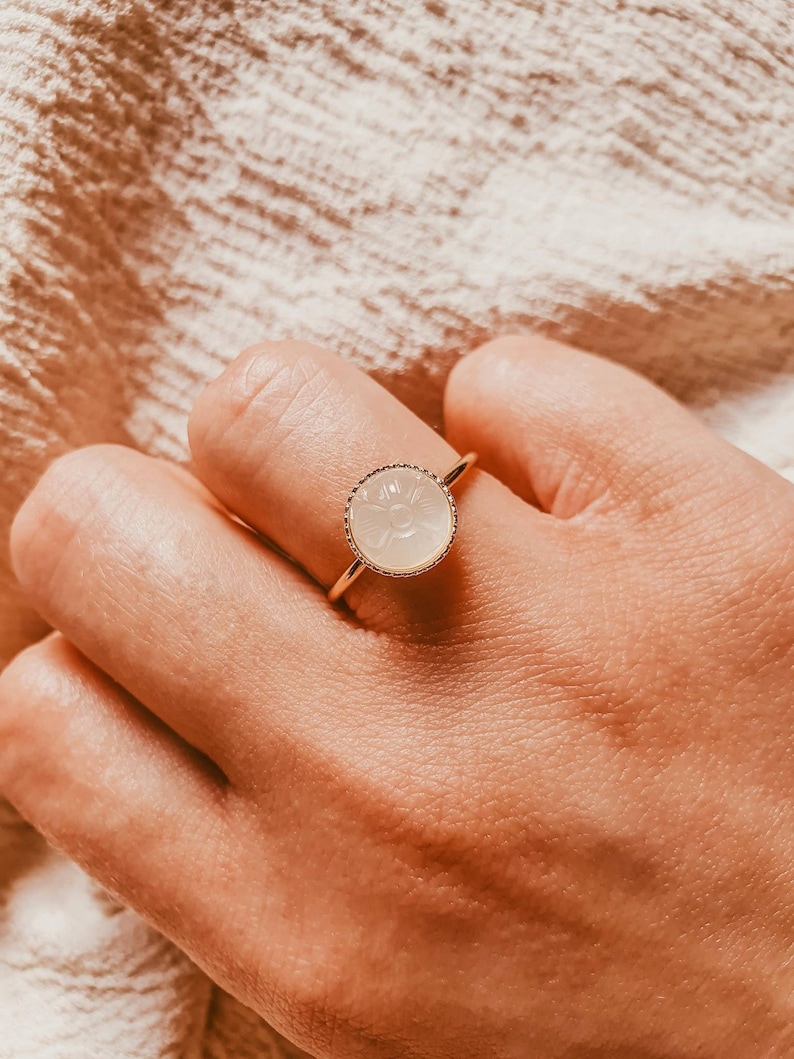 May include: A gold ring featuring a white, carved gemstone set in a gold bezel. The stone has a floral design.