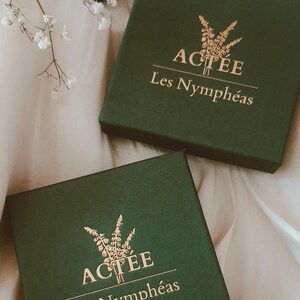 May include: Three green boxes with gold lettering that reads "ACTEE Les Nympheas". The boxes are on a white surface.