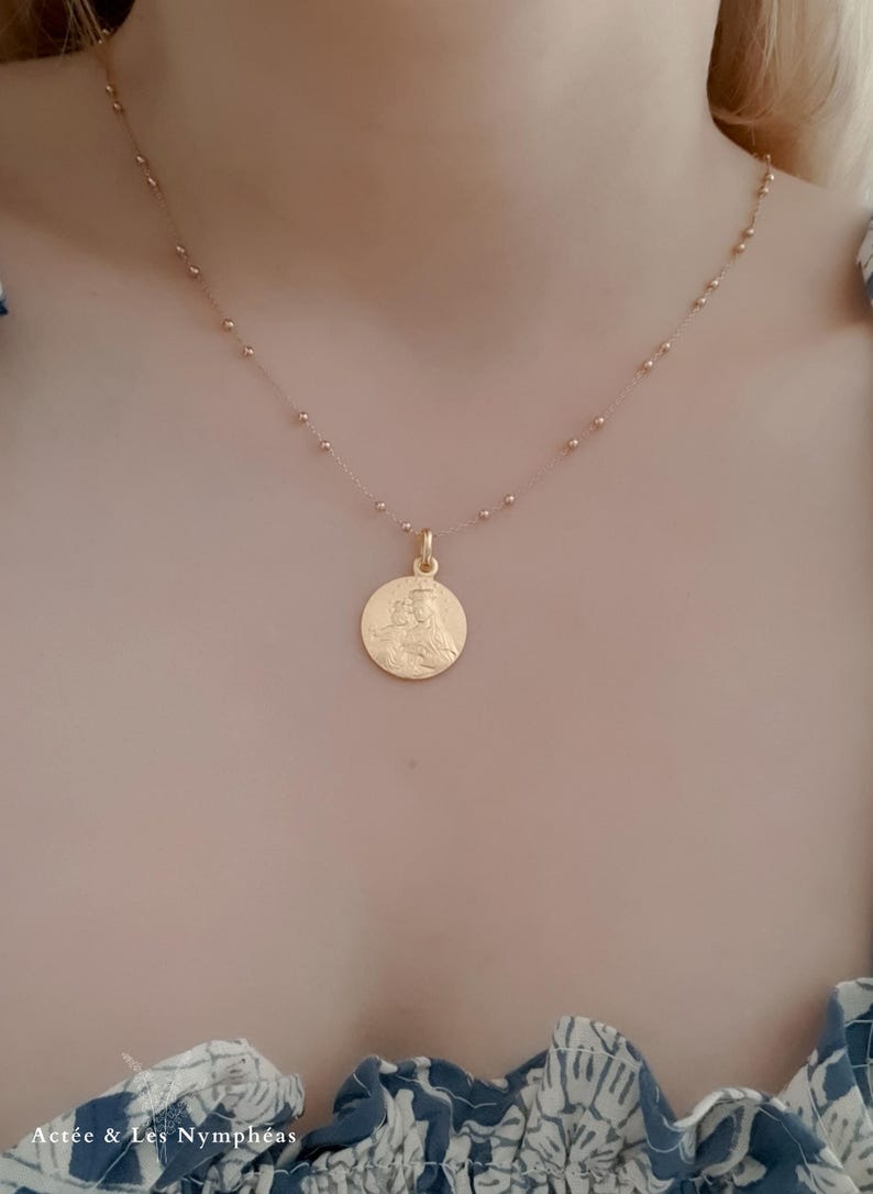 May include: A gold chain necklace with a round pendant featuring a detailed image of a woman. The chain is made of small, evenly spaced beads.