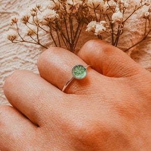 May include: A silver ring with a green, sparkly, round stone set in the center.
