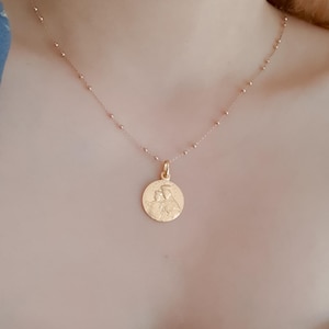 May include: A gold chain necklace with a round pendant featuring a detailed image of a mother and child.