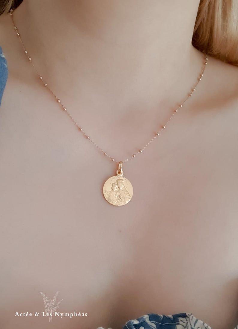 May include: A gold chain necklace with a round pendant featuring a detailed image of a mother and child.