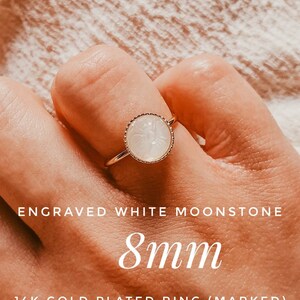 May include: A gold plated ring featuring an 8mm white moonstone with an engraved floral design. The ring is marked 14k.
