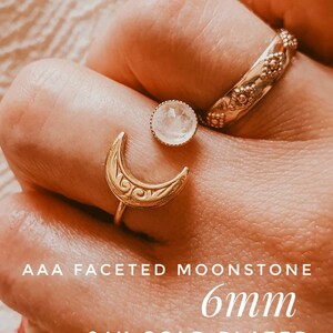 May include: A close-up of three gold-plated rings. One ring is a crescent moon design, another is a band with floral details, and the third is a 6mm faceted moonstone. The text reads "AAA FACETED MOONSTONE" and "24K GOLD PLATED".