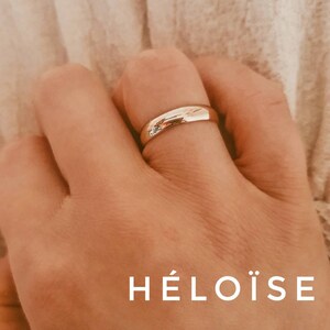 Pu&ograve; includere: Un anello a fascia d'oro sul dito di una persona. La parola "H&Eacute;LO&Iuml;SE" &egrave; scritta sotto l'anello.