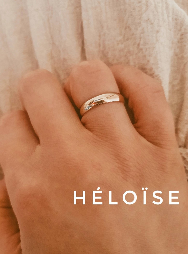 Pu&ograve; includere: Un anello a fascia d'oro sul dito di una persona. La parola "H&Eacute;LO&Iuml;SE" &egrave; scritta sotto l'anello.