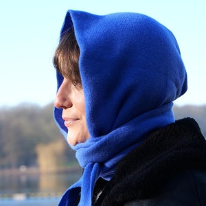Könnte beinhalten: Eine leuchtend blaue Strickkapuze, die den Kopf bedeckt und um den Hals gewickelt wird, mit glatter Textur und langen Enden, die unter dem Kinn gebunden werden. Das Accessoire besteht aus einem weichen, einfarbigen Stoff mit schlichtem Design.