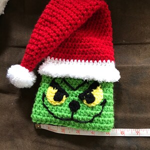 May include: Green crocheted Grinch character with yellow eyes and a red crocheted Santa hat with a white pom-pom.