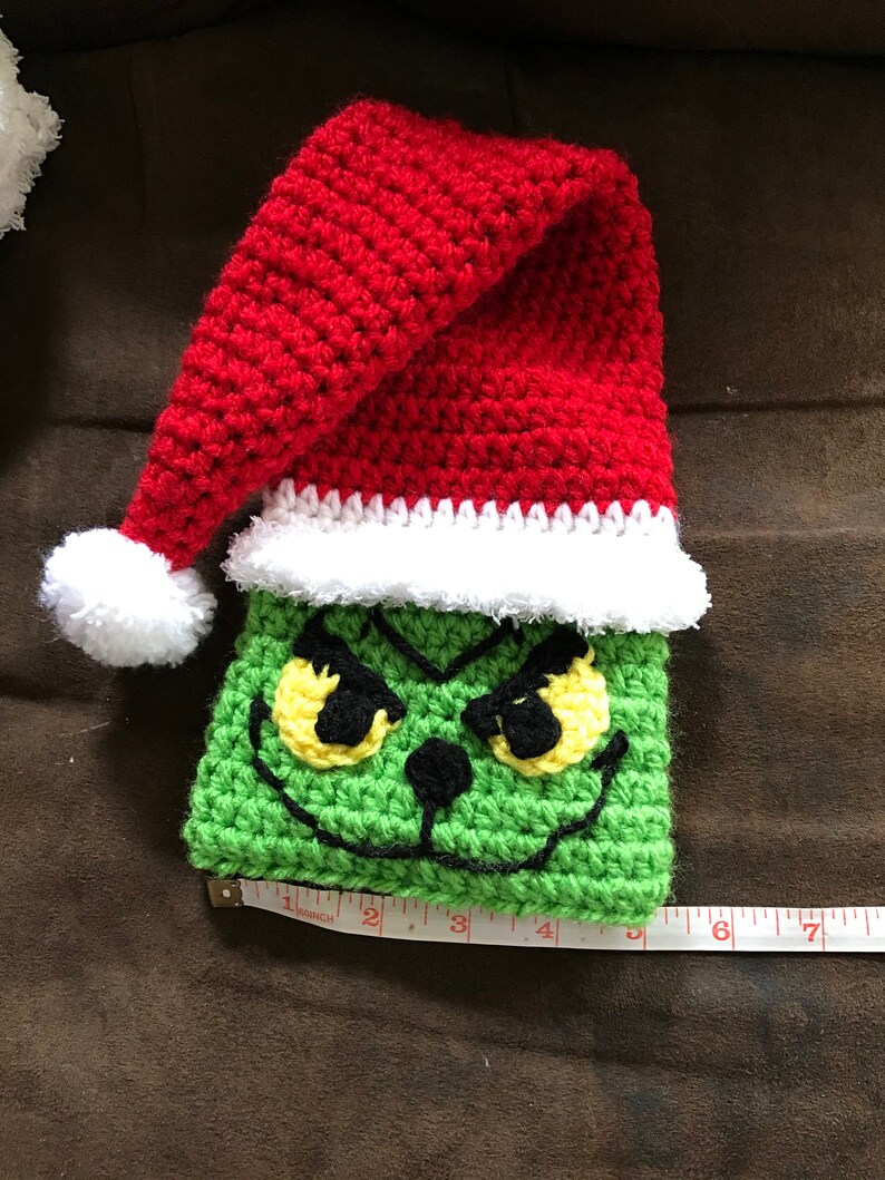 May include: Green crocheted Grinch character with yellow eyes and a red crocheted Santa hat with a white pom-pom.