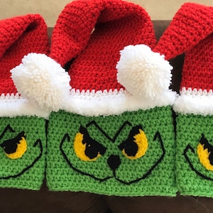 May include: Three crocheted Grinch hats with red and white Santa hats on top. The Grinch faces are green with yellow eyes and black eyebrows.