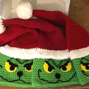 May include: Three crocheted Grinch hats with white pom-poms. The hats are red and green with a white trim and feature a Grinch face with yellow eyes and a black nose.