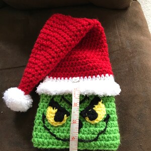 May include: Green crocheted Grinch stocking with a red crocheted Santa hat and white pom-pom. The stocking is 6 inches tall.