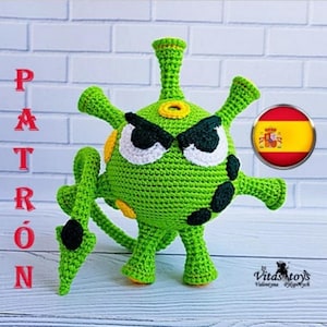 May include: A green crocheted virus-shaped toy with black and white angry eyes, yellow accents, and multiple appendages. The word "PATRÓN" is written vertically in red letters. A Spanish flag emblem is also present.