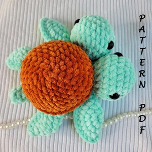 May include: A handmade crochet turtle in shades of orange and teal. The turtle has a textured shell and head, with flipper-like limbs. Black bead eyes are visible. The image includes the text "PATTERN PDF".