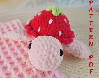 May include: A handmade crochet turtle with a strawberry-shaped shell. The turtle is primarily pink, with a red strawberry shell featuring white accents and a green stem. The text "PATTERN PDF" is visible in red.