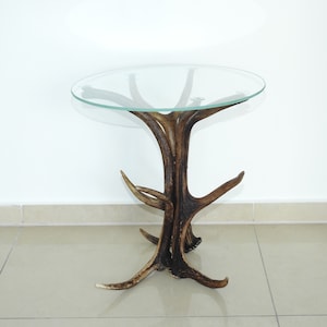 May include: A round glass table top sits on a base made of antlers. The antlers are arranged in a tree-like shape, with the points of the antlers facing outwards.