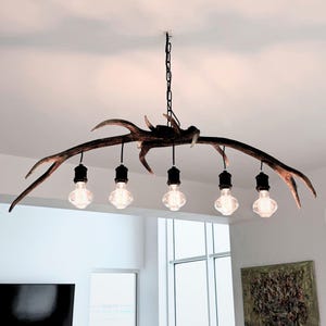May include: A striking antler chandelier with five Edison-style light bulbs. The fixture is suspended from a black chain and has a natural brown and tan colour scheme. The bulbs hang from black cords, creating a unique lighting design.