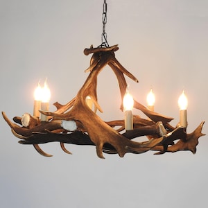 May include: A rustic antler chandelier with five candle-style lights. The chandelier is made of brown antlers and has a metal chain for hanging. The lights are lit, casting a warm glow.