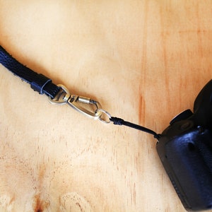 May include: A black leather camera strap with a silver carabiner clip attached to a black Canon camera.