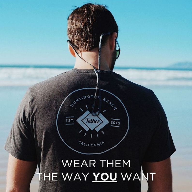 K&ouml;nnte beinhalten: Eine Person tr&auml;gt ein schwarzes T-Shirt mit einem wei&szlig;en Kreislogo, auf dem "Huntington Beach Est. 2015 California" und ein Diamant mit dem Wort "Tether" stehen. Der Text "Wear them the way you want" ist unter dem Logo gedruckt.