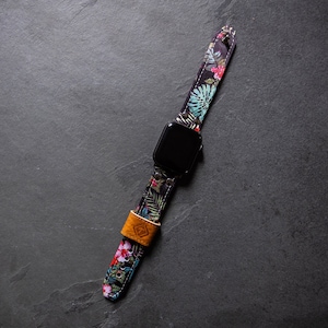 Può includere: Un Apple Watch nero con un cinturino a fantasia floreale. Il cinturino ha un cinturino in pelle marrone con una fibbia in metallo.