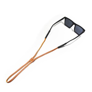 K&ouml;nnte beinhalten: Ein braunes Lederband mit schwarzen verstellbaren Enden zum Halten von Sonnenbrillen.