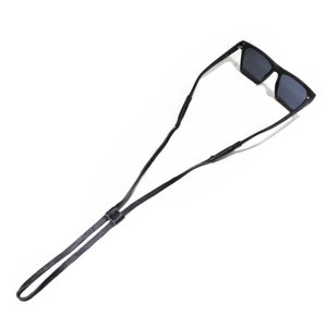 K&ouml;nnte beinhalten: Schwarzes Leder-Sonnenbrillenband mit verstellbarer L&auml;nge. Das Band ist so konzipiert, dass es die Sonnenbrille sicher um den Hals h&auml;lt.